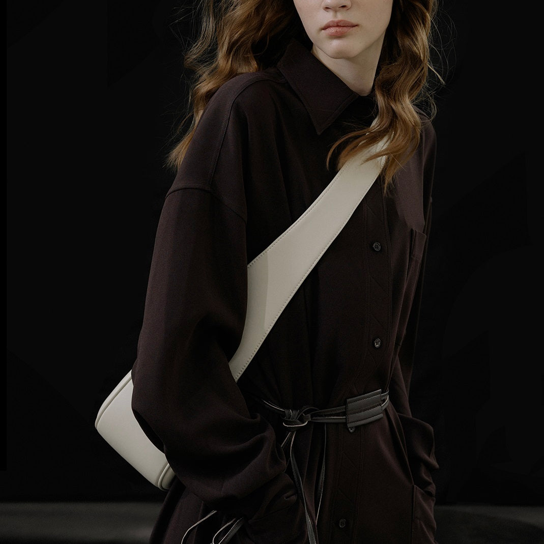 Person wearing a dark coat with a white strap over the shoulder against a black background