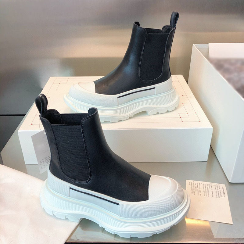 Black and white Chelsea boots on a reflective surface with a box in the background