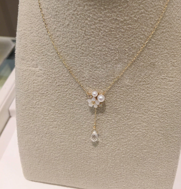 Delicate gold necklace with a floral pendant and clear crystal on a gray surface