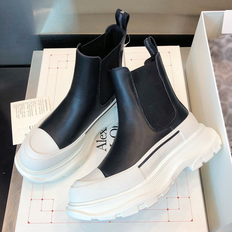 Black Chelsea boots with white soles on a design paper background