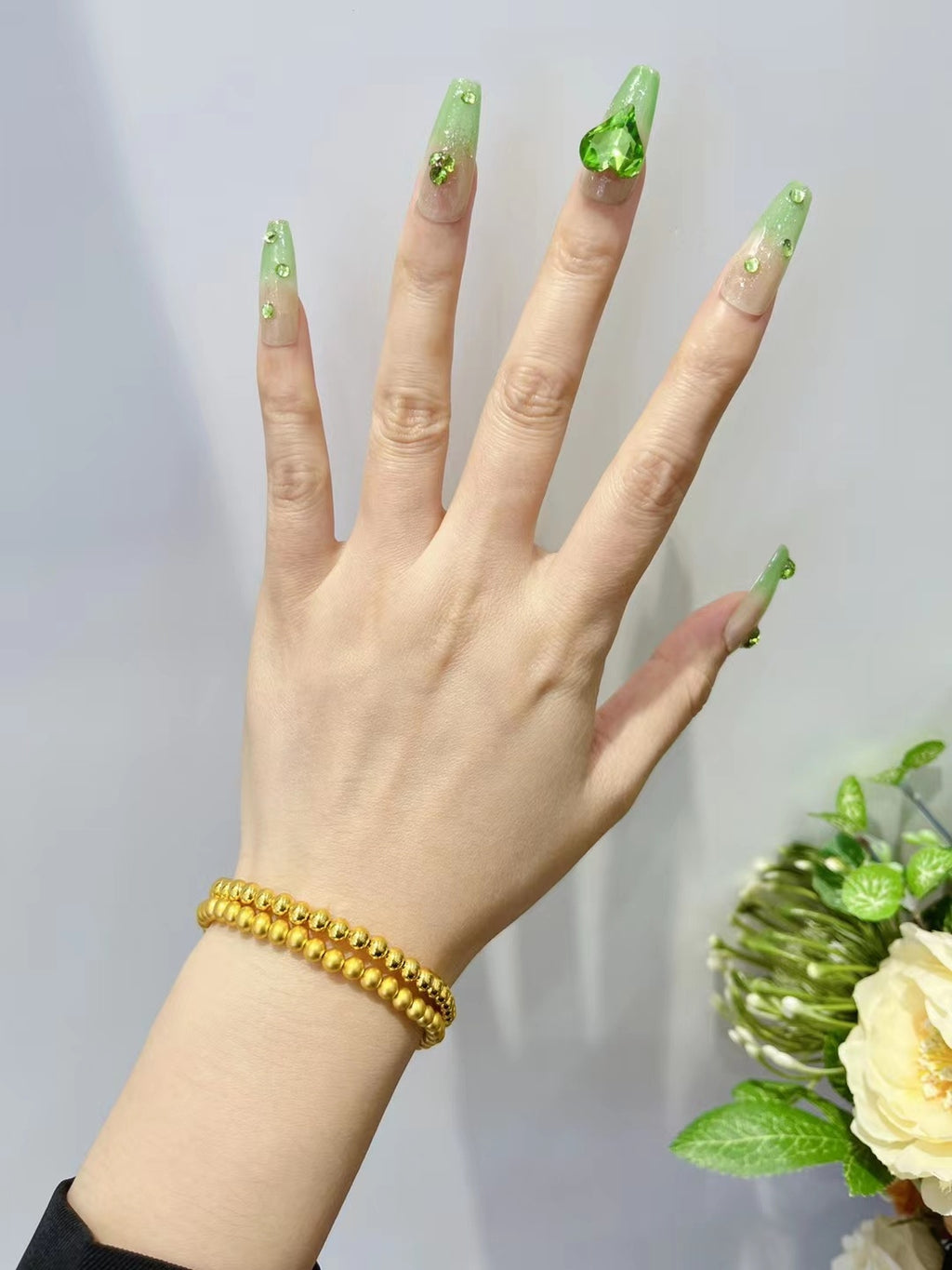 Hand with green nail polish and gold bracelet, with a blurred background
