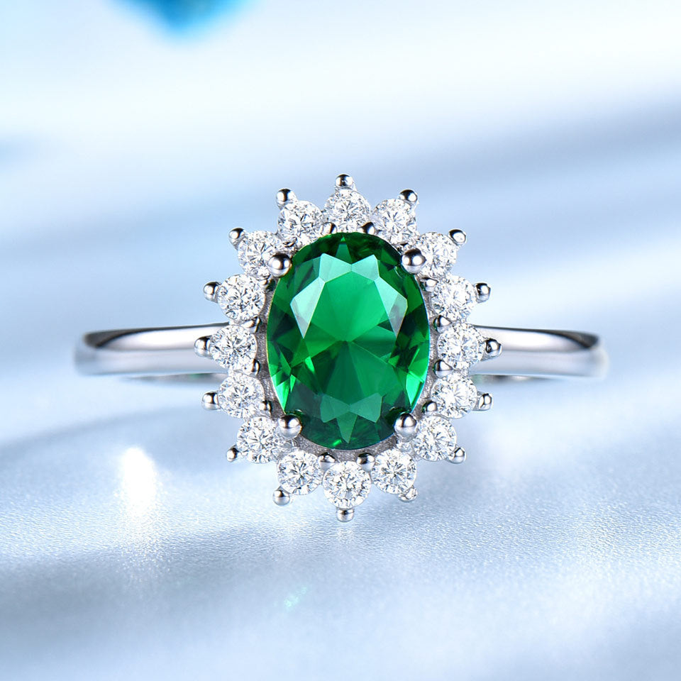 Ring with a green gemstone and diamond-studded halo on a light blue background