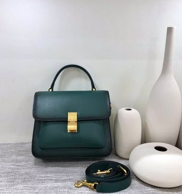 Green handbag with gold accents on a gray surface with white vases in the background