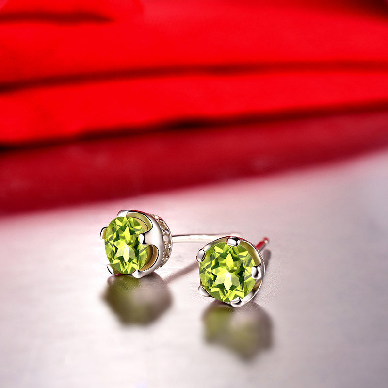 Green gemstone stud earrings on a reflective surface with a red background
