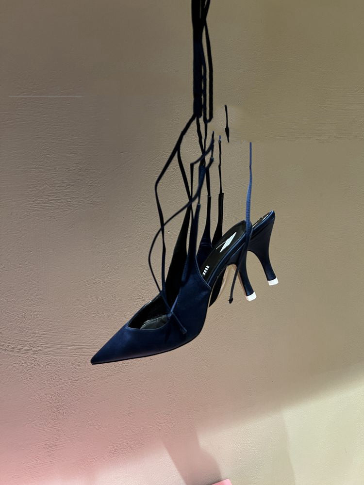 Blue high-heeled shoes with thin straps hanging against a plain background