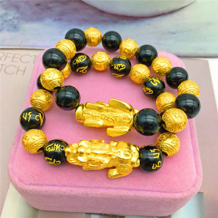 Gold and black beaded bracelet with lion-like figures on a pink jewelry box.