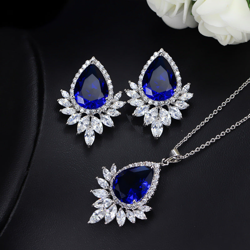 Jewelry set with blue teardrop stones on a dark surface with white flowers.