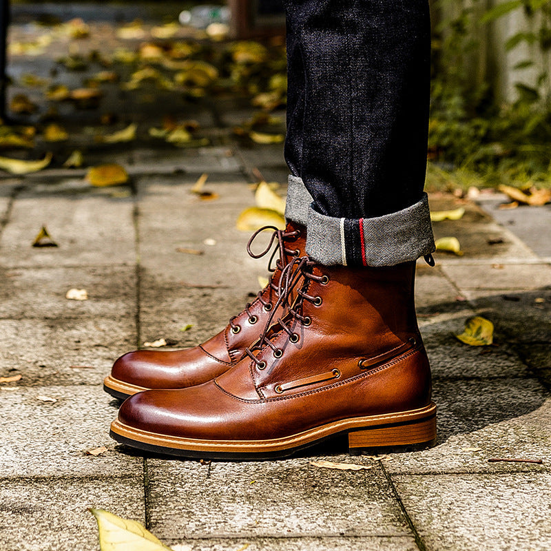 Brown leather boots worn with dark jeans on a wooden floor with autumn leaves.