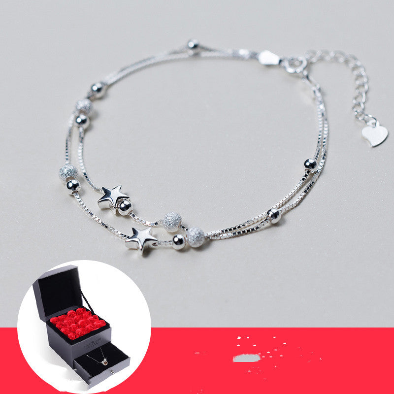 Silver bracelet with star and heart charms on a gray background, with a small inset showing a jewelry box with red roses.
