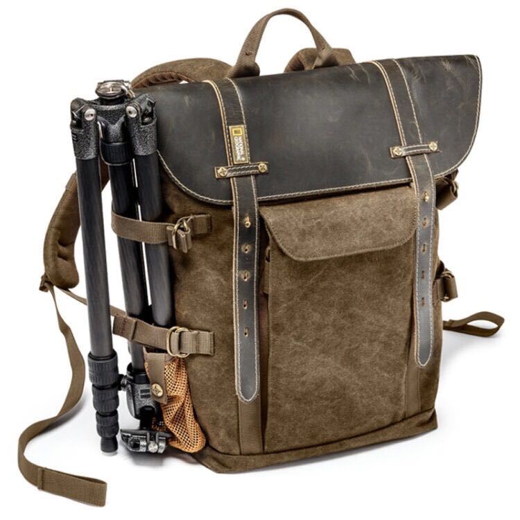 Brown leather and canvas backpack with a camera tripod attached on a white background