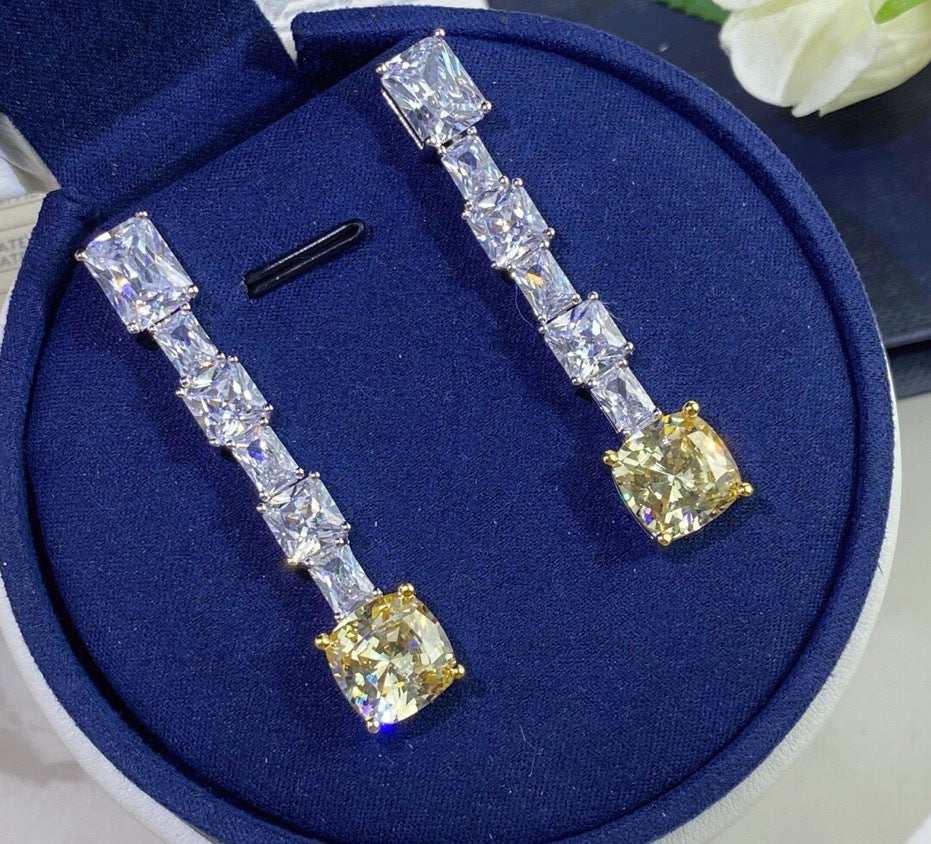 Diamond earrings on a blue cushion with a white flower in the background