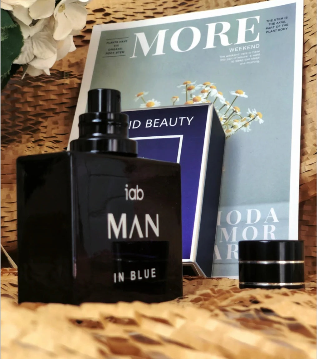 Black perfume bottle labeled 'iab MAN IN BLUE' on a magazine with floral decorations.