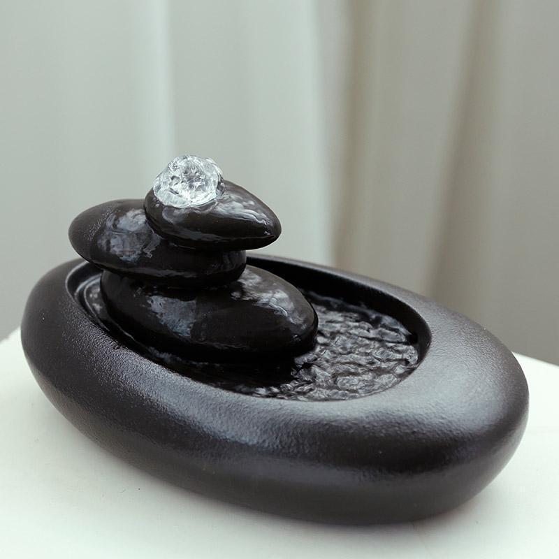 Decorative black stone water fountain with a diamond on top against a neutral background