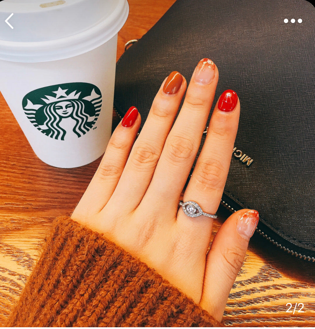 Hand with red nail polish wearing a ring next to a Starbucks cup on a wooden table.