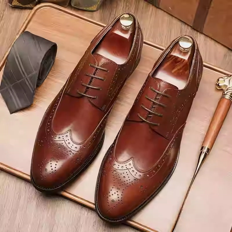 Brown leather dress shoes on a wooden surface with a tie and walking cane.