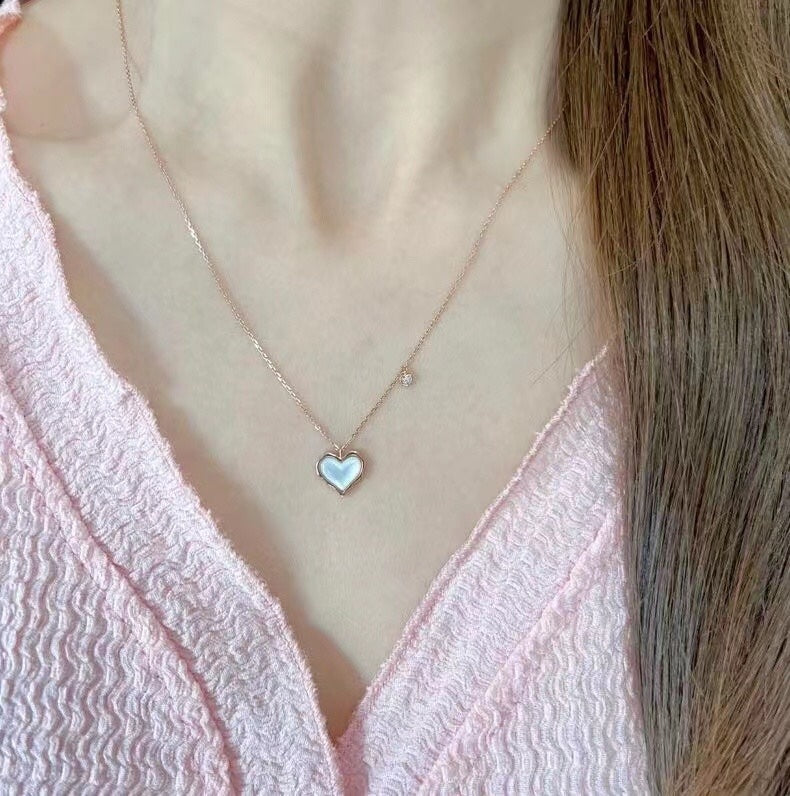 Necklace with a heart-shaped pendant worn by a person in a pink top.