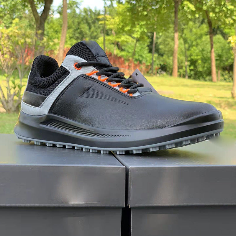 Gray golf shoe with black and orange accents on a metal surface with a green outdoor background