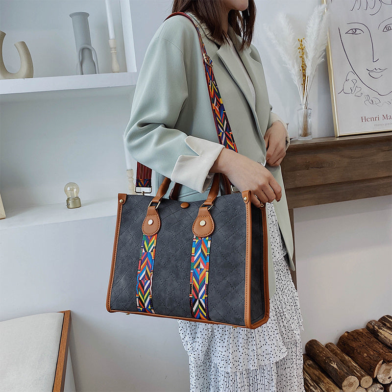Person holding a gray handbag with colorful strap in a home setting