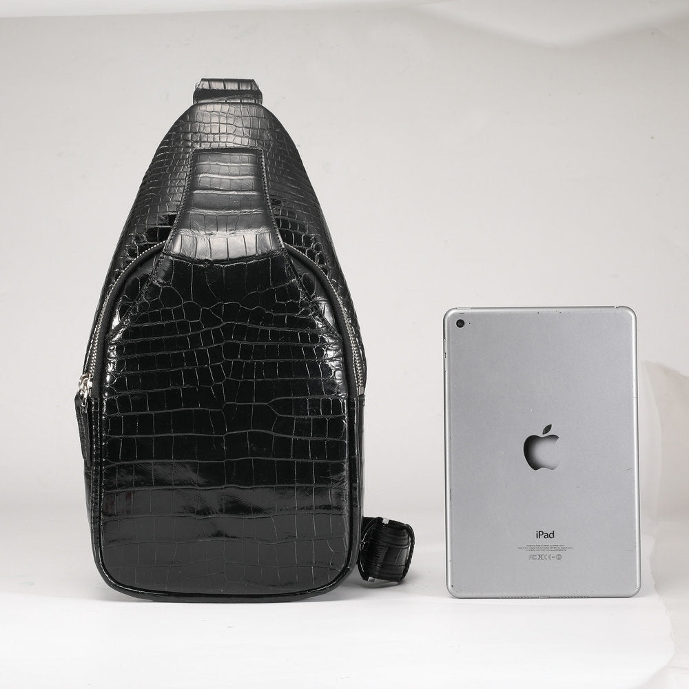 Black crocodile-patterned sling bag next to a silver iPad on a white background