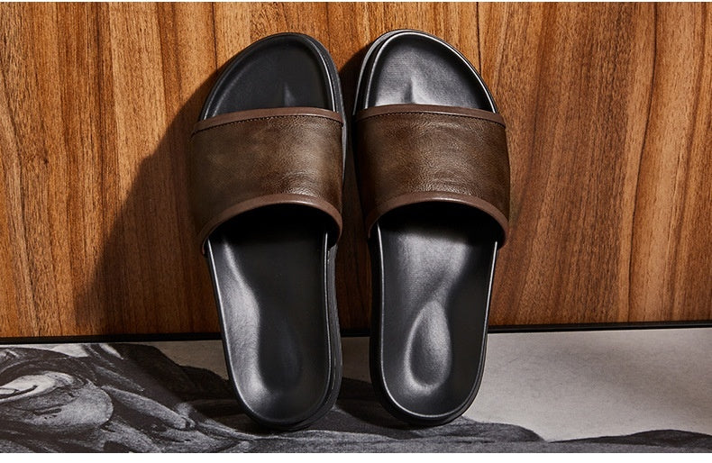 Pair of brown slides with black soles on a wooden floor.