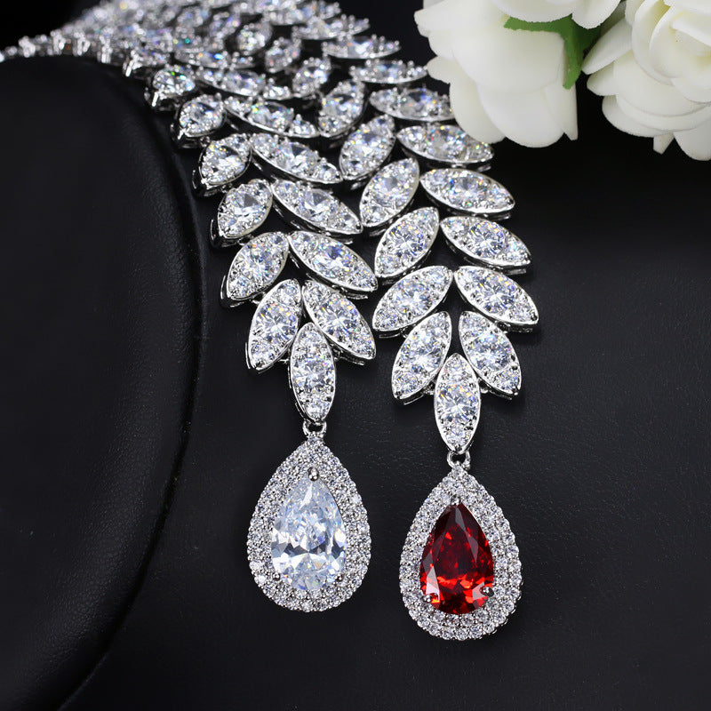 Pair of teardrop-shaped earrings with clear and red gemstones on a black background.
