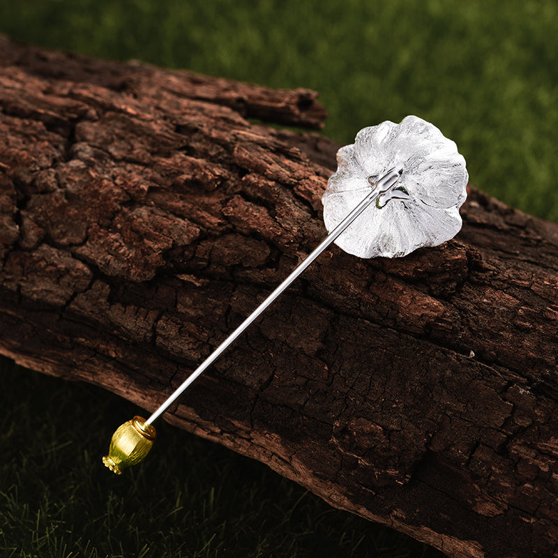 Silver flower-shaped stickpin with gold accent on a wooden log