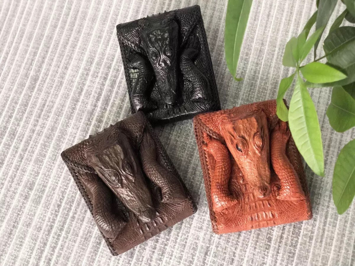Three leather wallets in black, brown, and red on a textured surface with a plant in the corner.