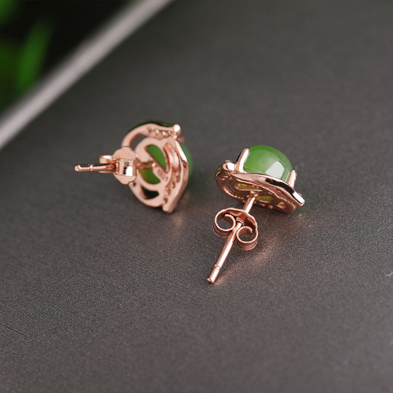 Rose gold earrings with green gemstones on a dark surface