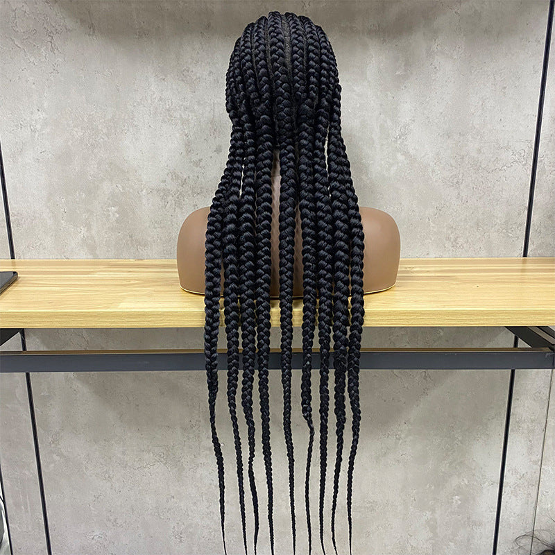 Black braided hair extensions on a wooden table against a gray wall.