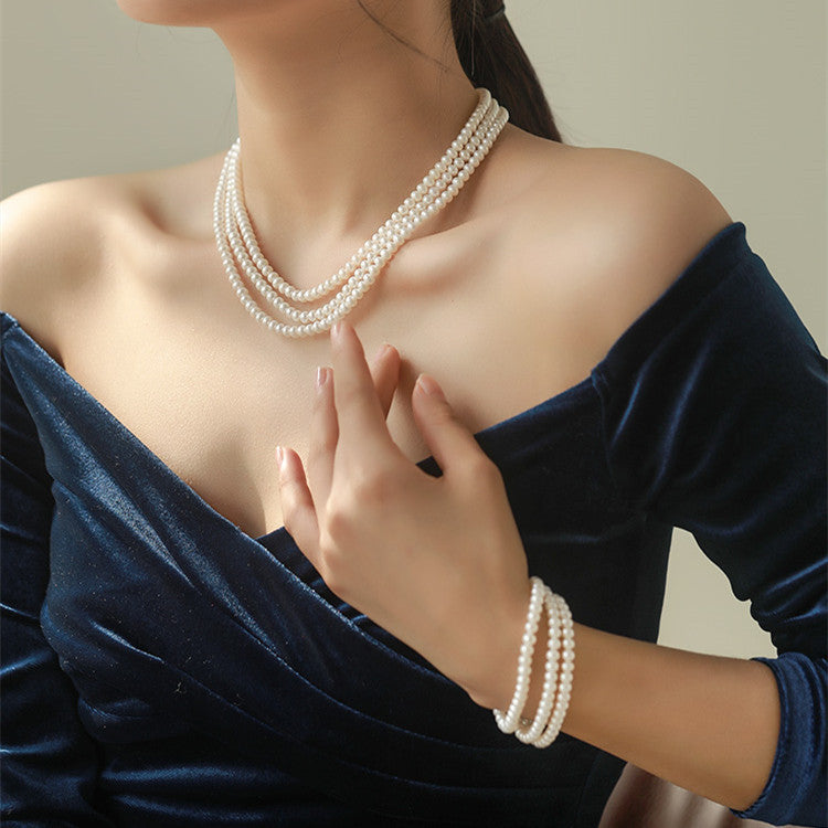 Woman wearing a pearl necklace and bracelet against a neutral background