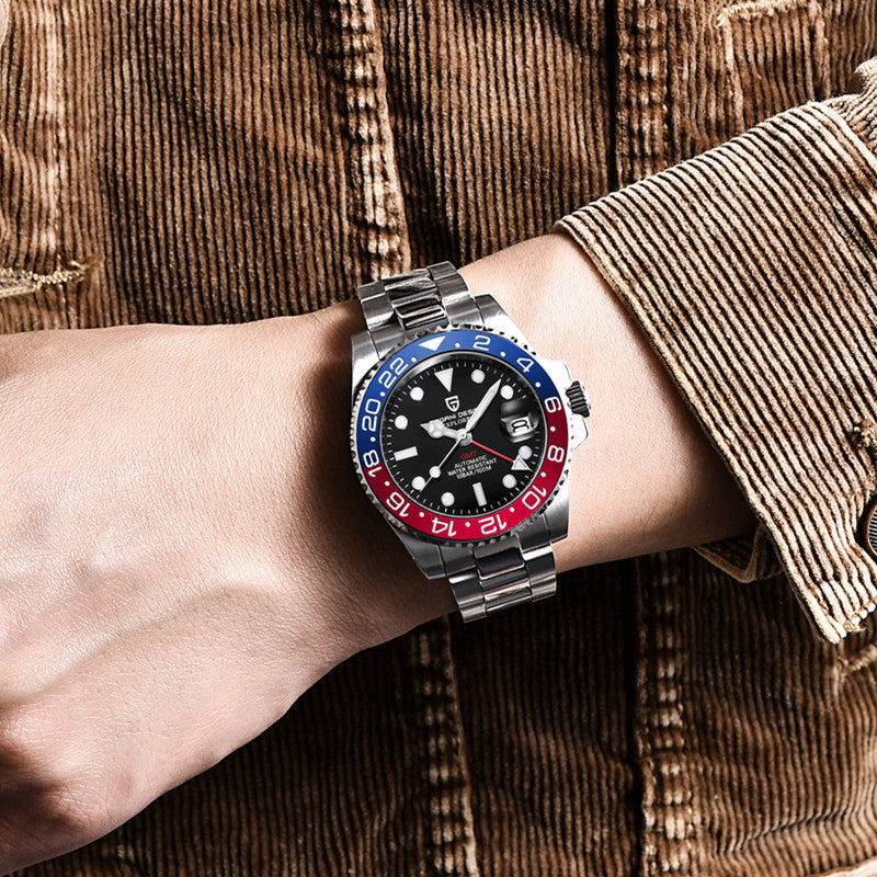 Watch with a black face, red and blue bezel on a wrist wearing a brown corduroy jacket.