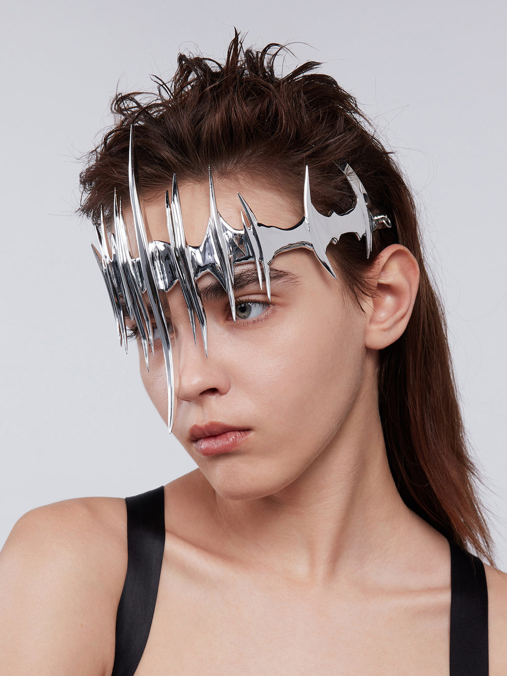 Person wearing a futuristic headpiece with metallic spikes on a plain background