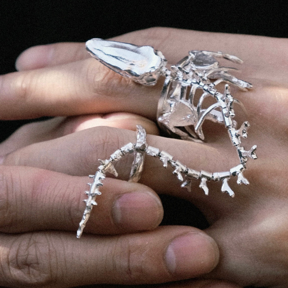 Silver skeleton ring on a hand against a dark background