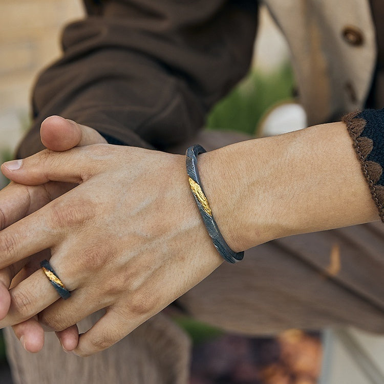 Close-up of a hand wearing a black leather bracelet with gold accents, held by another person.