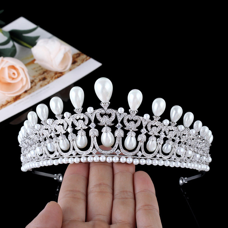 Silver tiara with pearls held by a hand against a black background