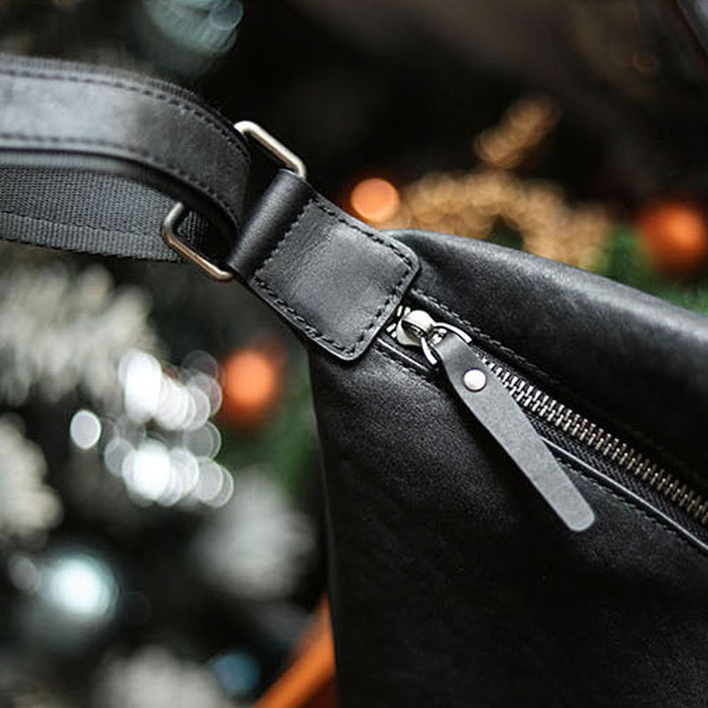 Close-up of a black leather bag with a zipper and strap against a blurred background