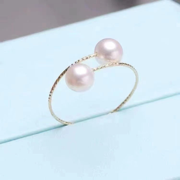 Gold ring with two pink pearls on a light blue surface