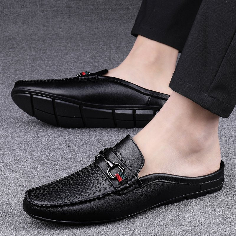 Black leather slip-on shoes worn by a person on a gray background