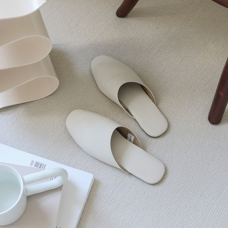 Pair of beige slippers on a light-colored floor with a white mug and magazine in the foreground.