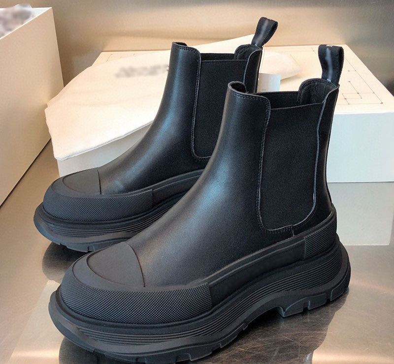 Pair of black Chelsea boots on a reflective surface with a neutral background