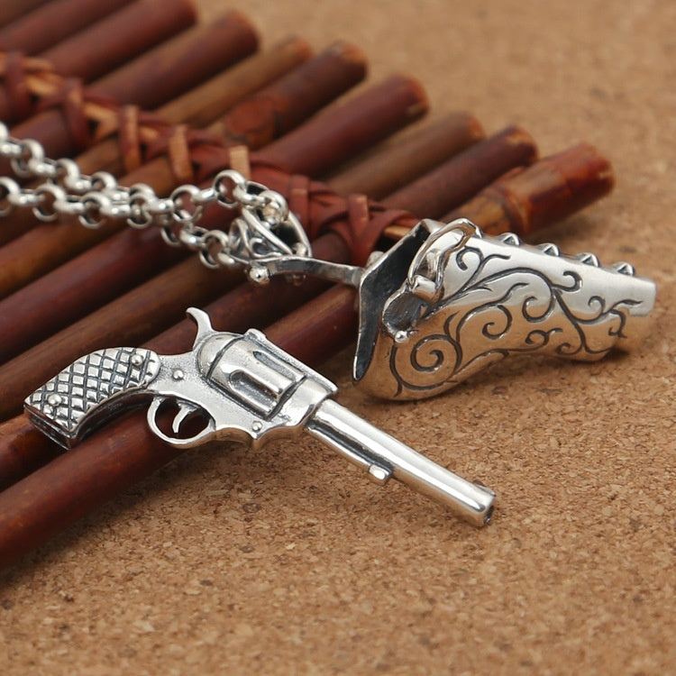 Silver revolver and dagger pendant on a chain against a brown background