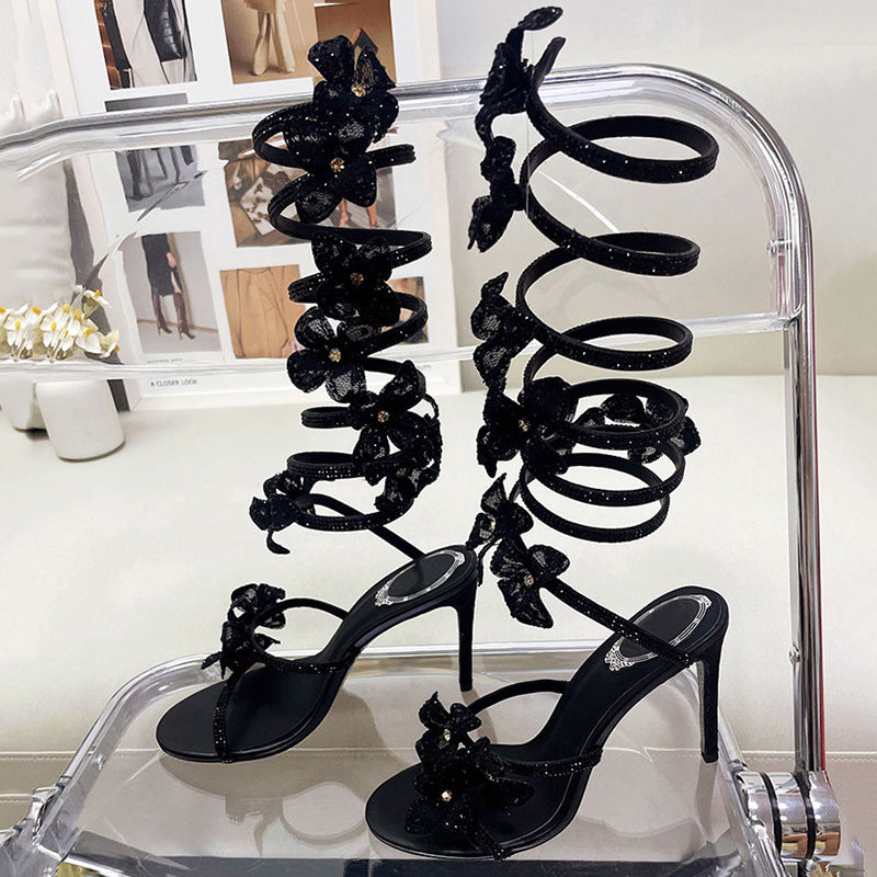 Black high-heeled sandals with floral designs on a clear stand.