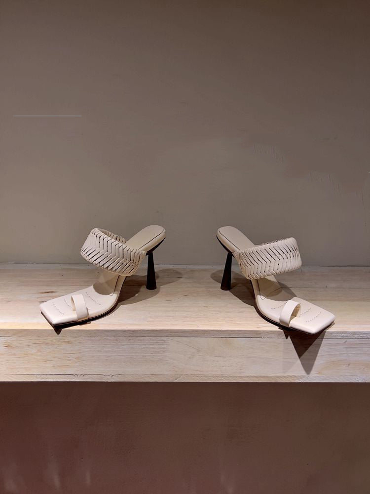 Pair of white woven sandals on a wooden surface with a neutral background