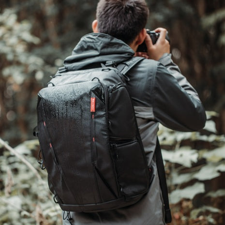 Person with a black backpack taking a photo in a forest