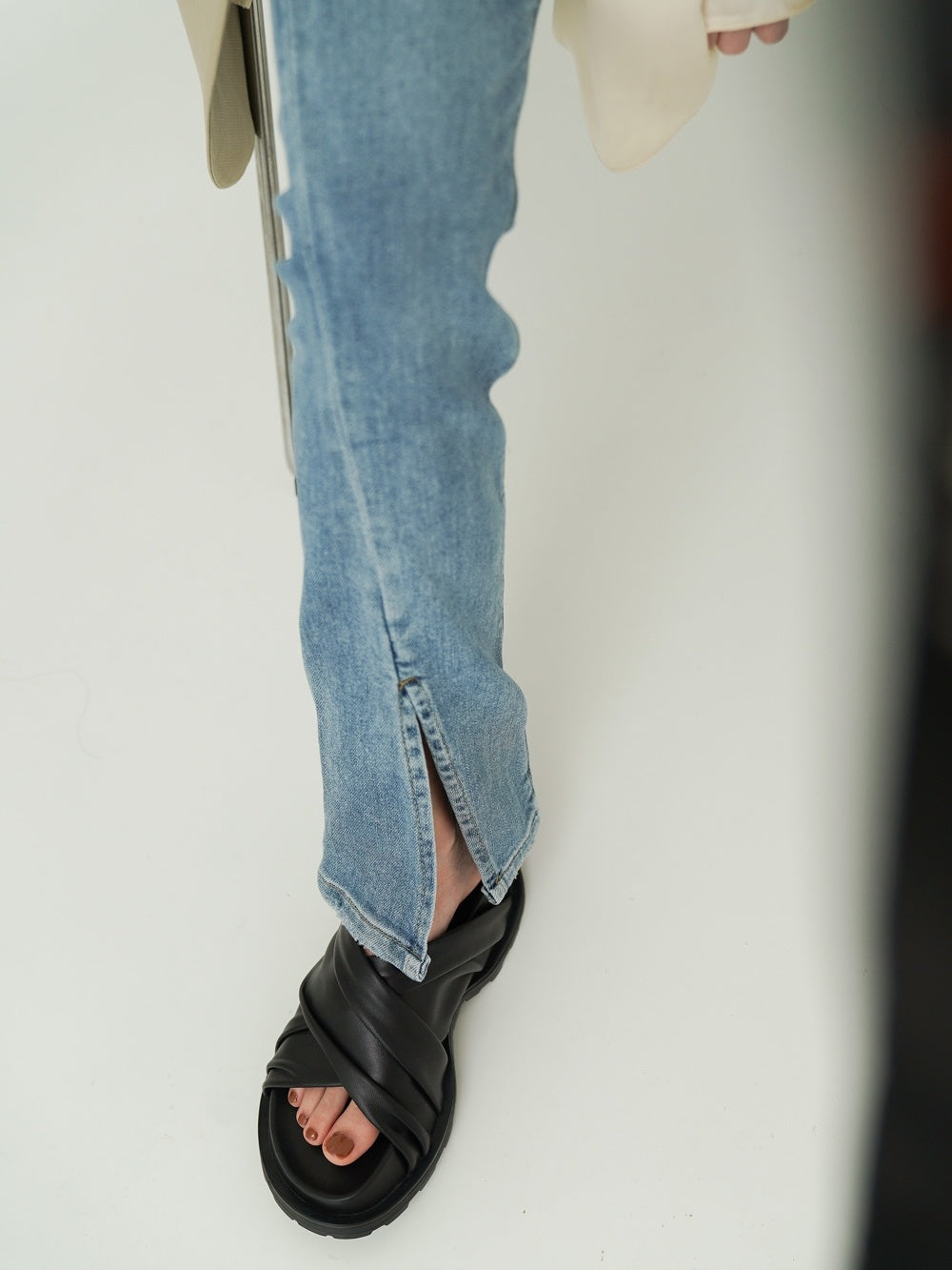 Person wearing blue jeans and black sandals on a white background