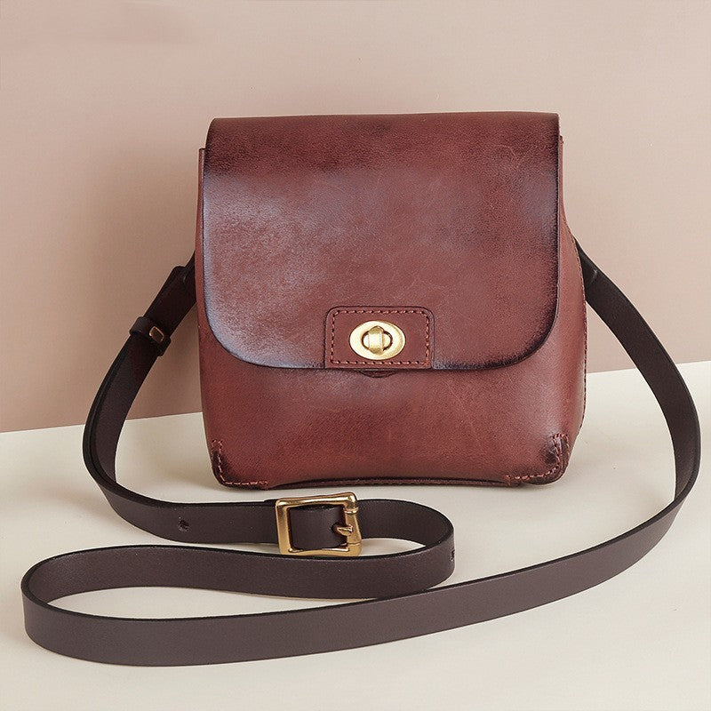 Brown leather bag with a gold buckle on a white surface with a beige background