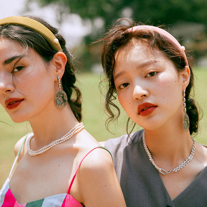 Two women wearing pearl necklaces outdoors with a blurred natural background