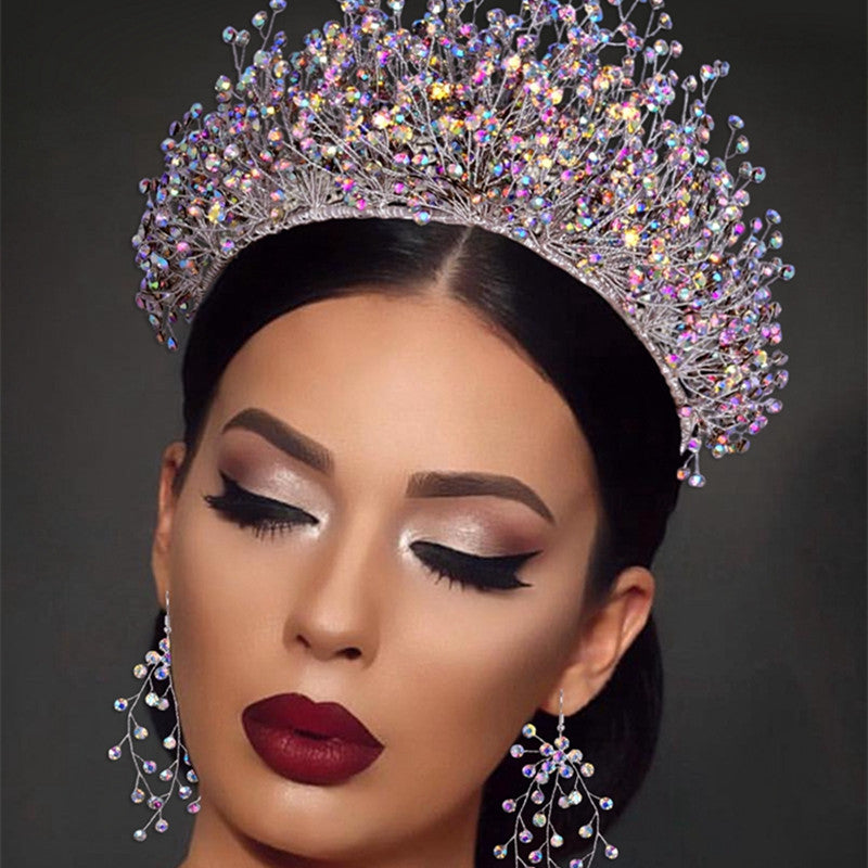 Woman wearing a sparkling tiara and earrings against a dark background