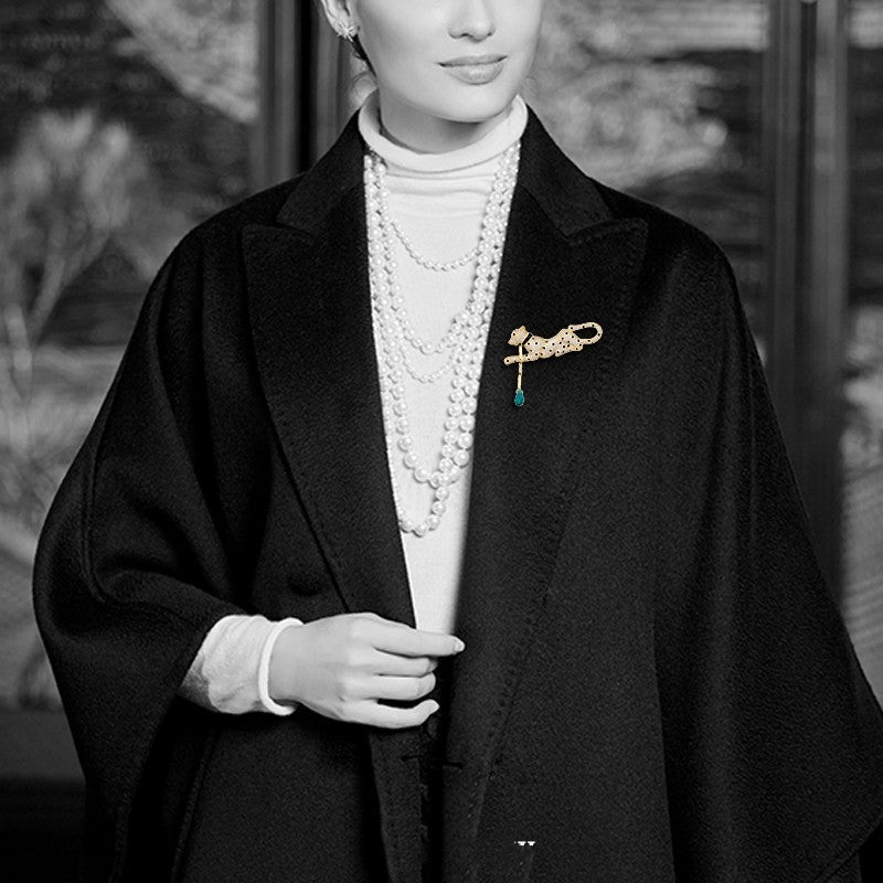Person wearing a black coat with a brooch, pearl necklace, and white gloves.