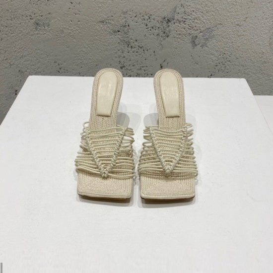 Pair of beige woven sandals on a white surface with a gray textured background